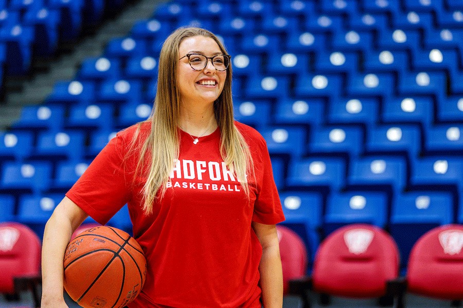 Graduating senior Ashlee Owens, who is also a student manager for the men's basketball team, smiles and holds a basketball while standing on the Dedmon Center's court.