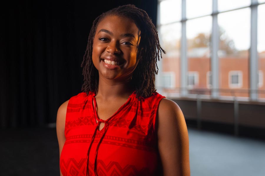 Graduating Senior Amiya Williams stands before a wall of windows in a campus building.