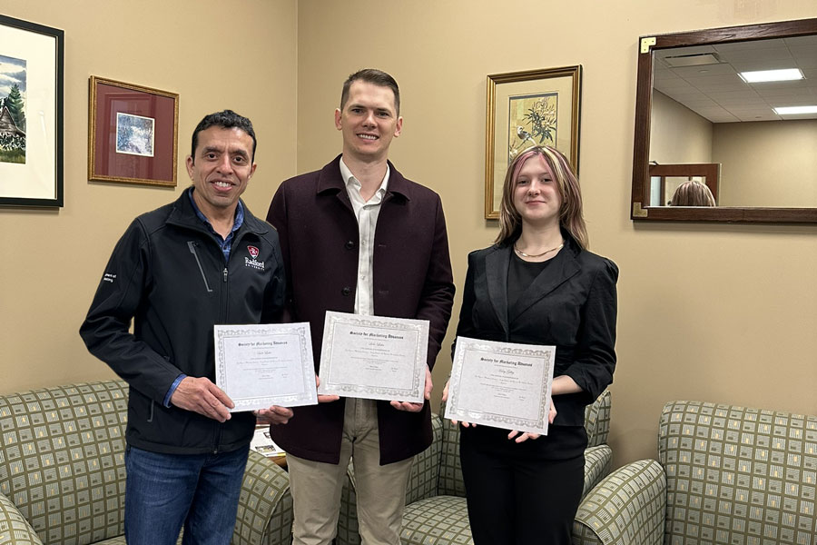 Two marketing faculty members and a sophomore business student pose with the award they recently received for a research paper. 