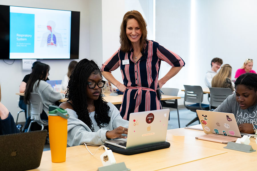 A College of Nursing faculty member works with a student on a laptop computer in a classroom