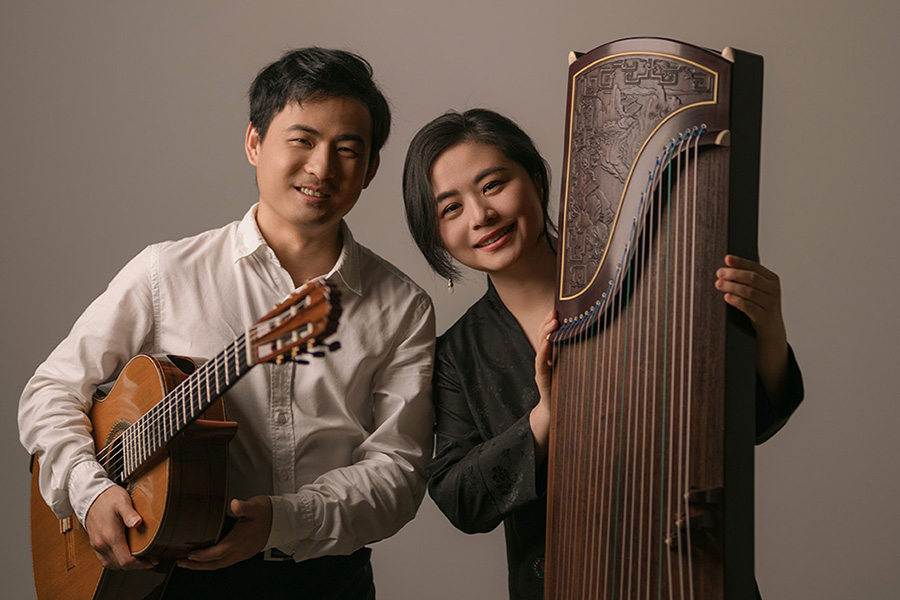 A man on left, Bin Hu, holds guitar next to a woman, Jing Xia, who holds a guzheng.