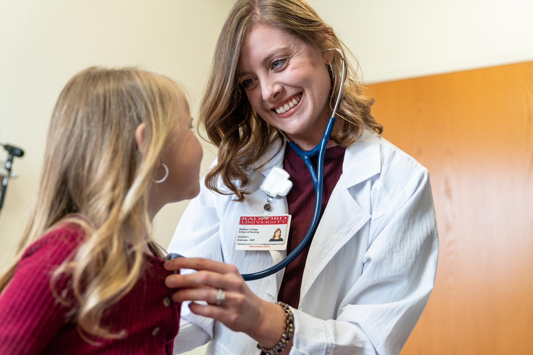 student in white lab coat and wearing a stethoscope hearing the heartbeat of a patient