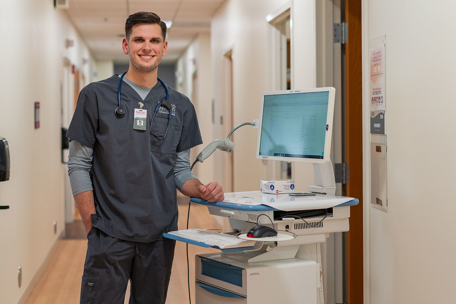 student in scrubs standing next to a mobile computer