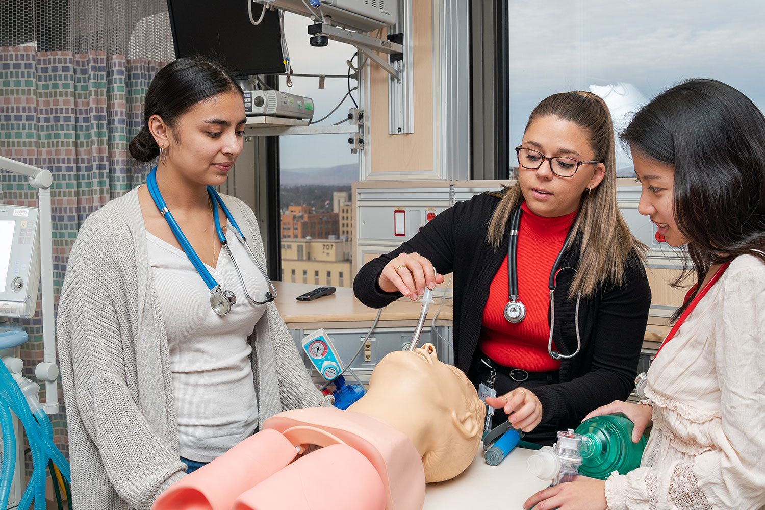 students gathered around a mannequin testing medical equipment