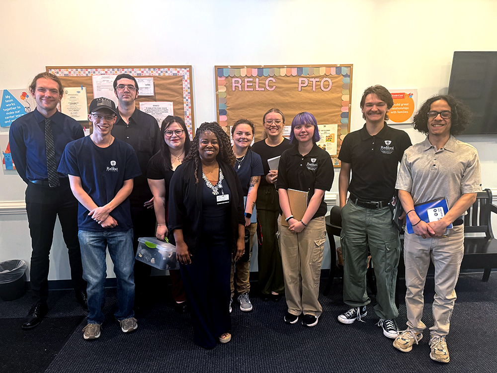 Krista Williams poses with music education students in an early learning classroom.