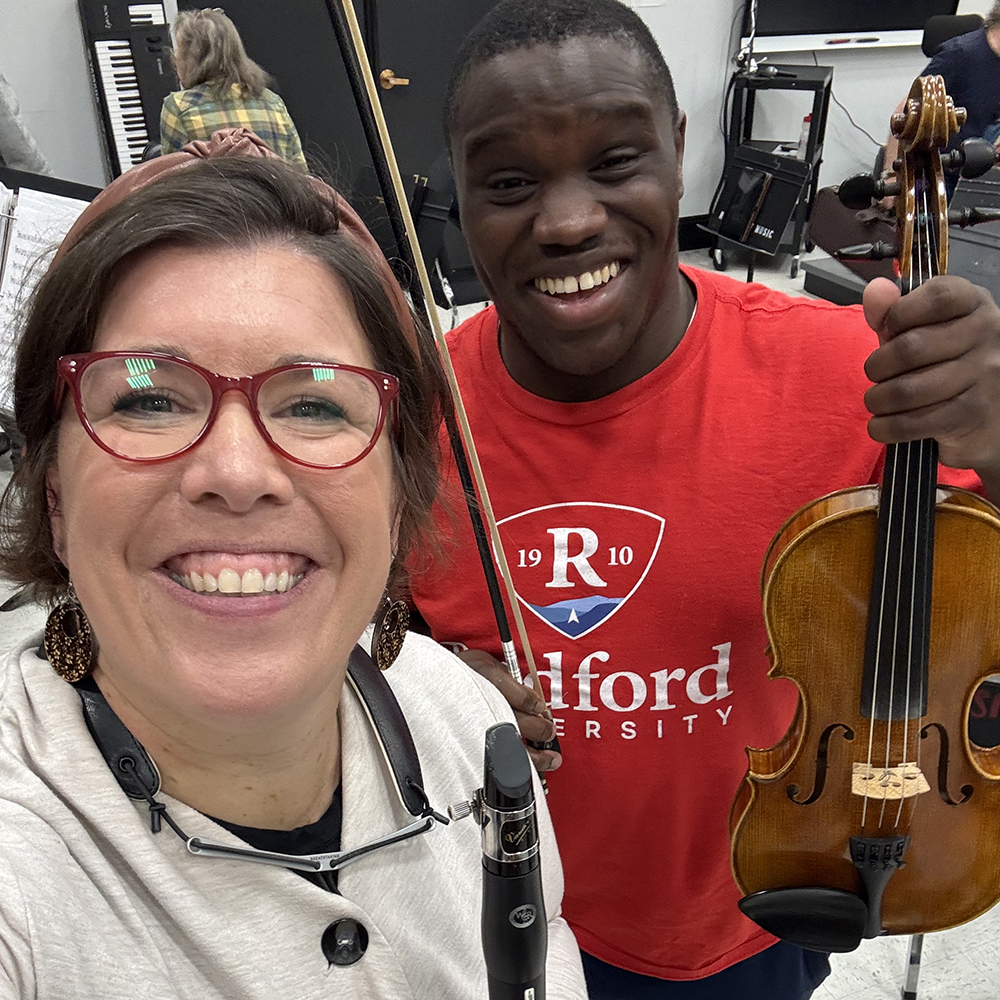 Woman, Michelle Smith-Johnson, with a student in red Radford university shirt holding a violin.