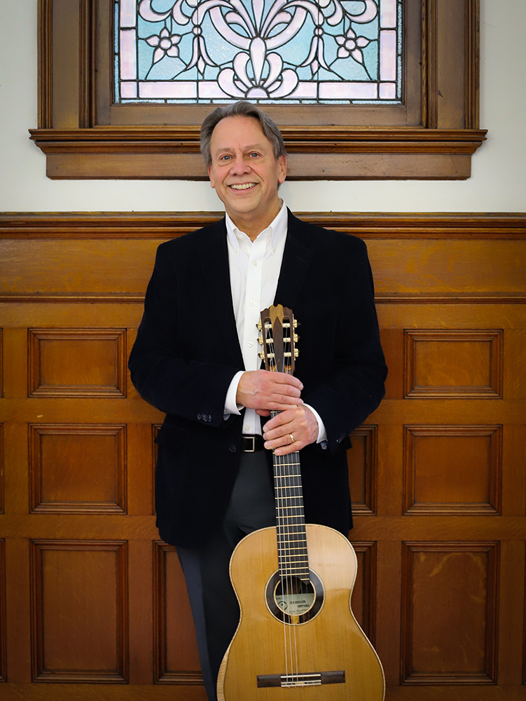 Man (Jim Piorkowski) stands with a guitar.