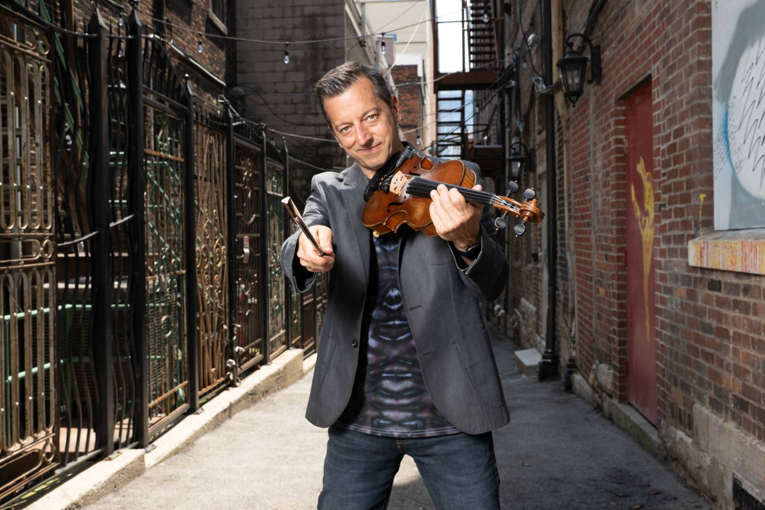 Bluegrass fiddle player Jason Carter in alley pointing with bow